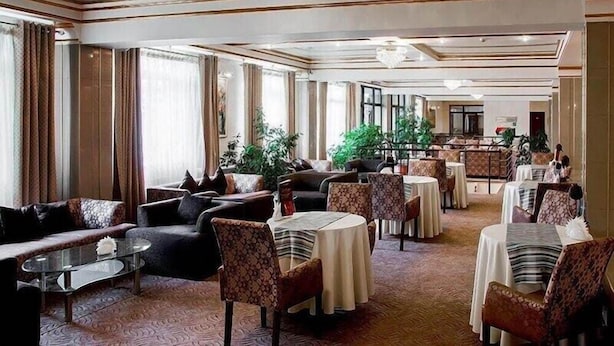 A spacious hotel lobby with multiple seating areas, including sofas and round tables, and a large plant in the center. - Astana International (Almaty)