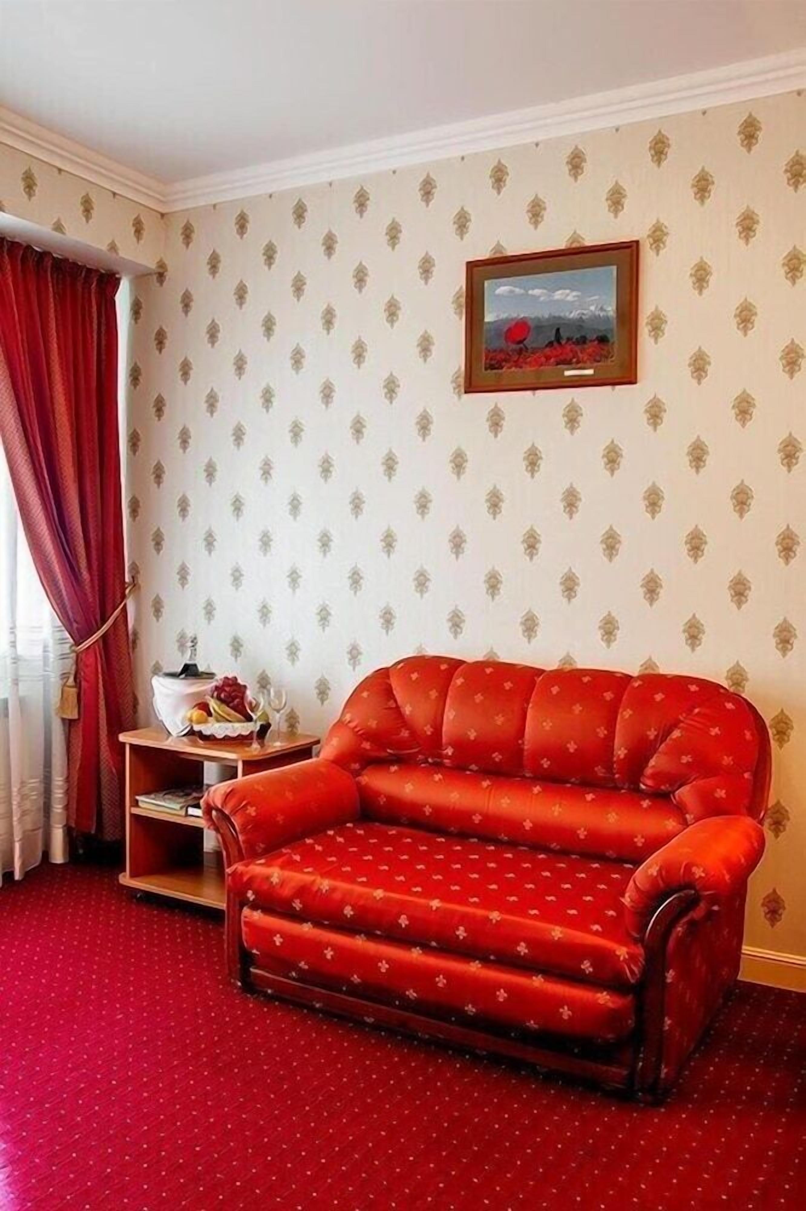 Une pièce avec un canapé rouge, une petite table sur laquelle se trouve un panier de fruits et un tableau encadré au mur.