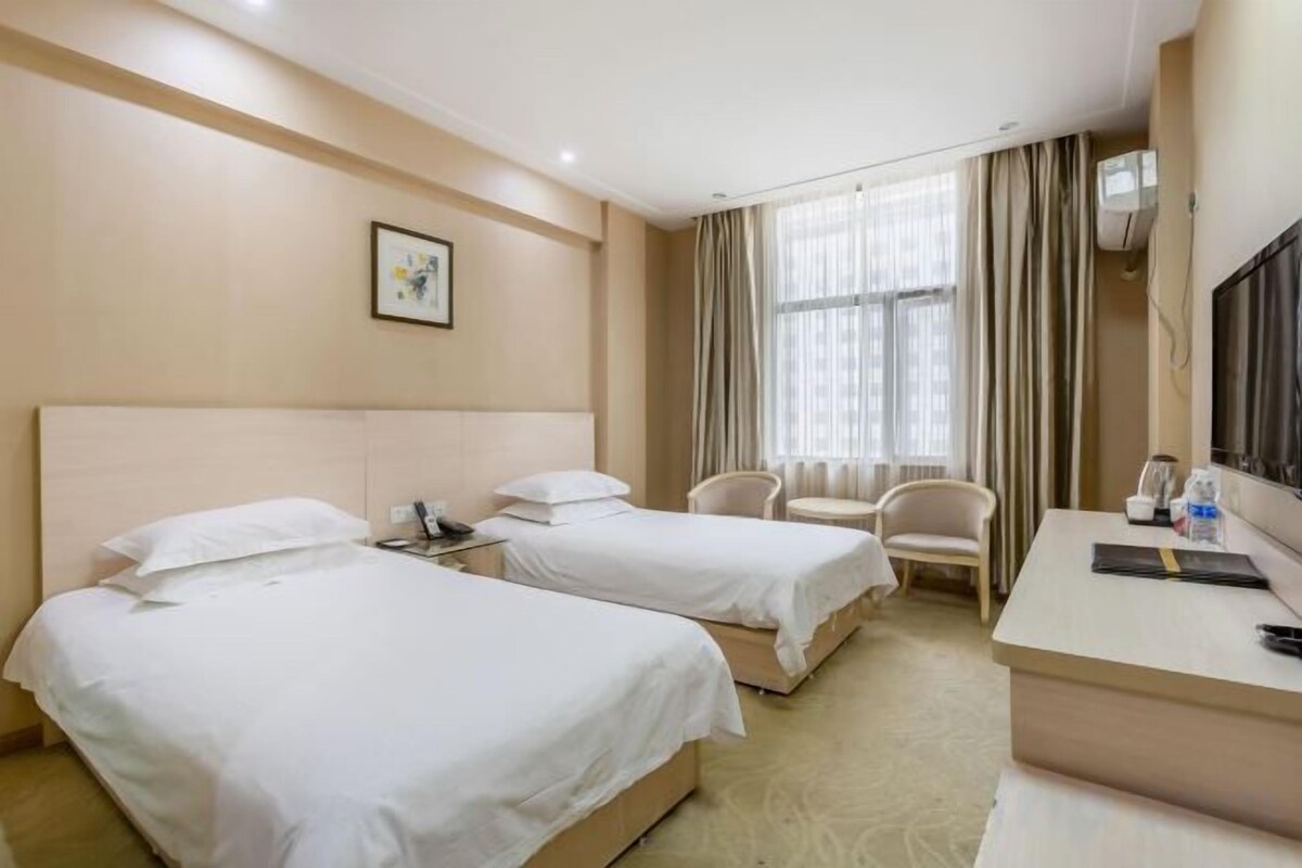 Habitación de hotel con dos camas, un escritorio, una silla, un televisor y una ventana con cortinas.