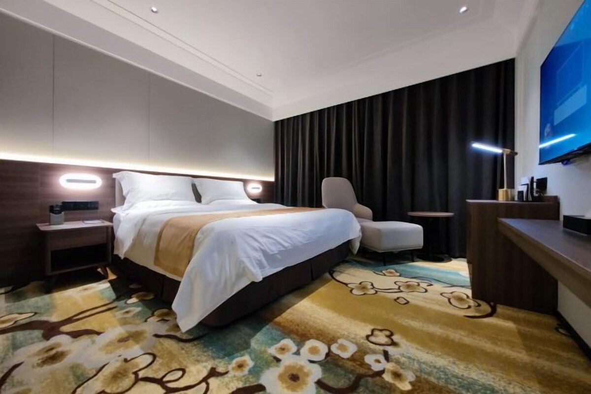 Habitación de hotel con una cama grande, un escritorio, una silla, un televisor y una mesita de noche.