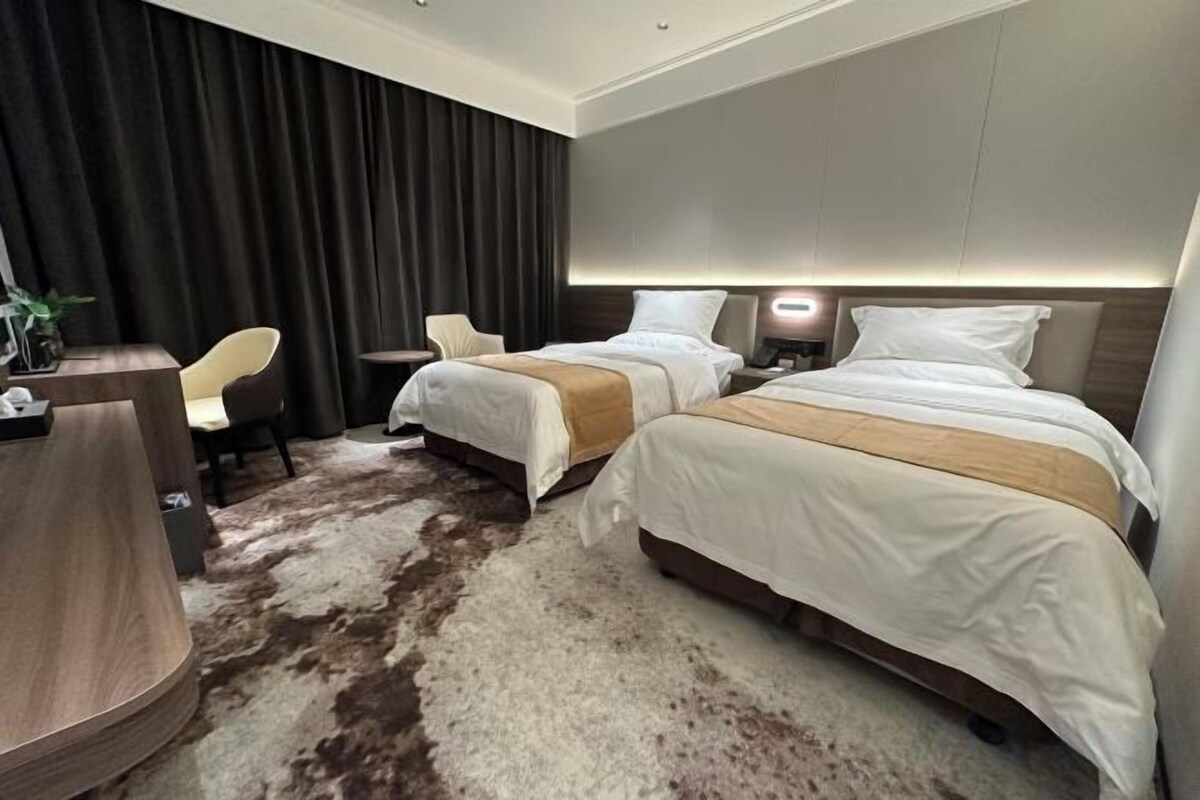 Habitación de hotel con dos camas, un escritorio, una silla y un amplio ventanal con cortinas.