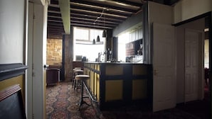 Een kamer met een kamerbreed tapijt, een bar met krukken, een stenen muur en een raam.