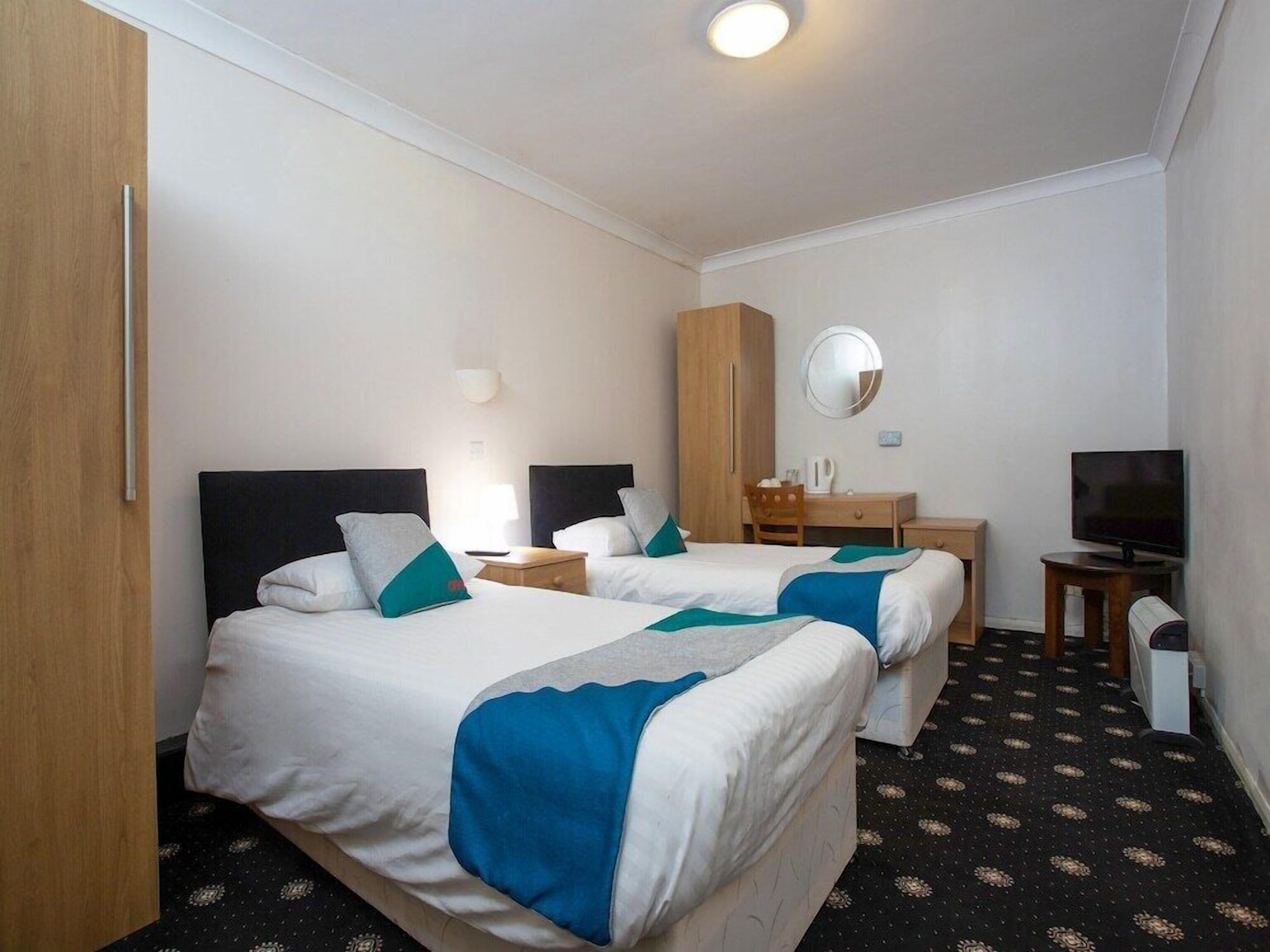 A hotel room with two beds, a desk, a TV, and a wardrobe.