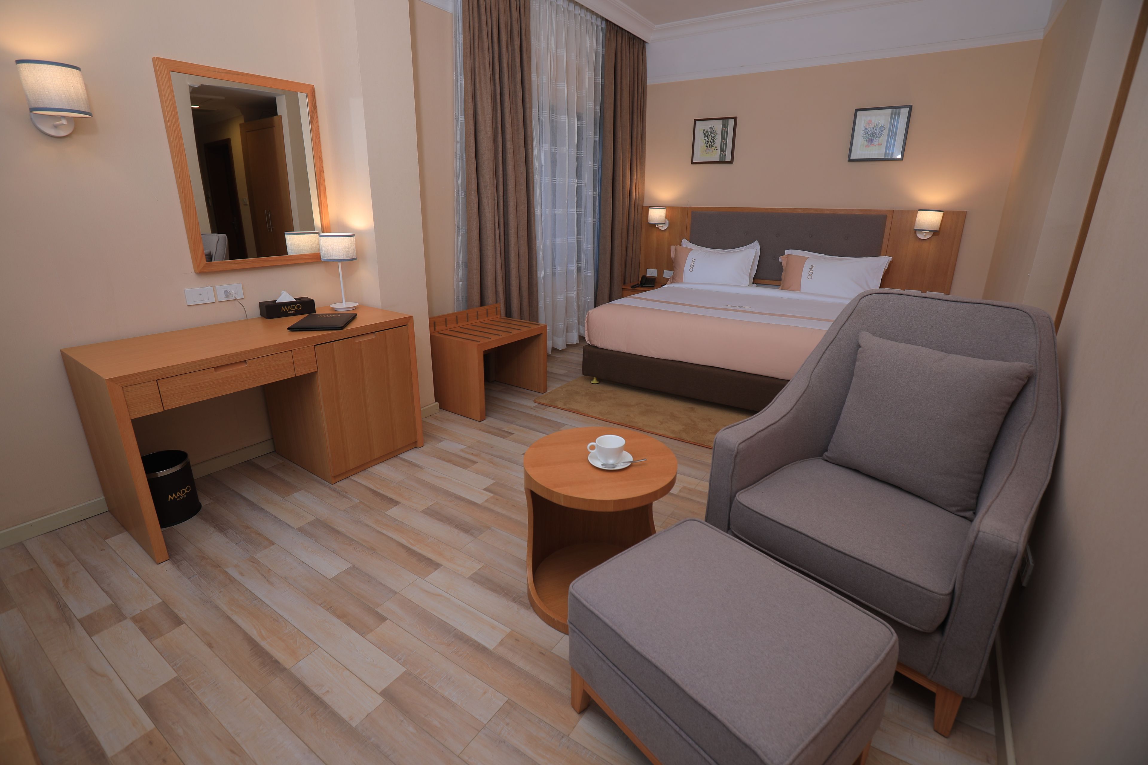 A hotel room with a bed, a desk, a chair, a small table, and a trash bin.