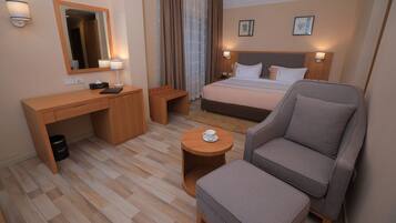 A hotel room with a bed, a desk, a chair, a small table, and a trash bin.