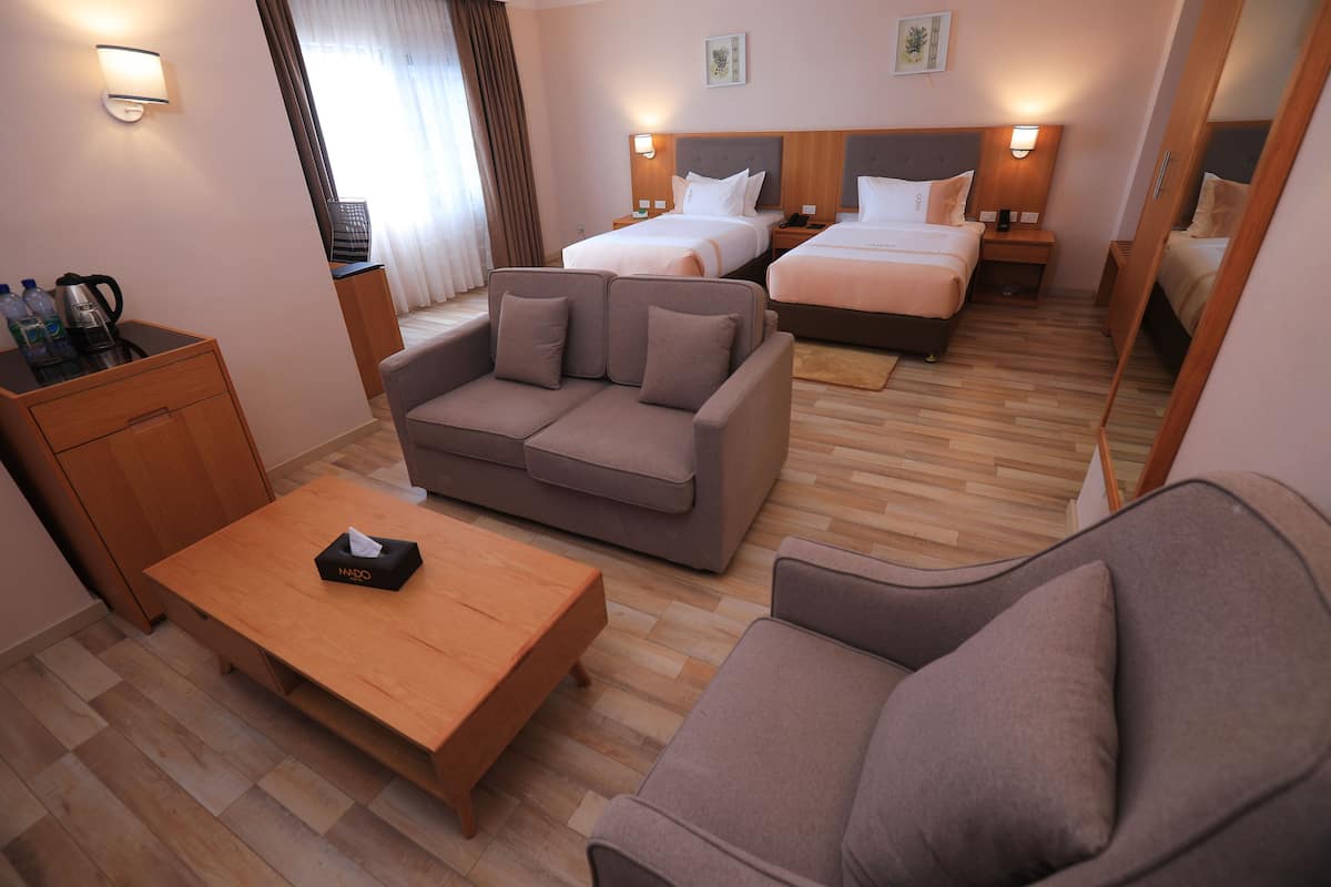 A hotel room with a sofa, a wooden coffee table, a bed with two pillows, a nightstand with a phone, and a mirror.