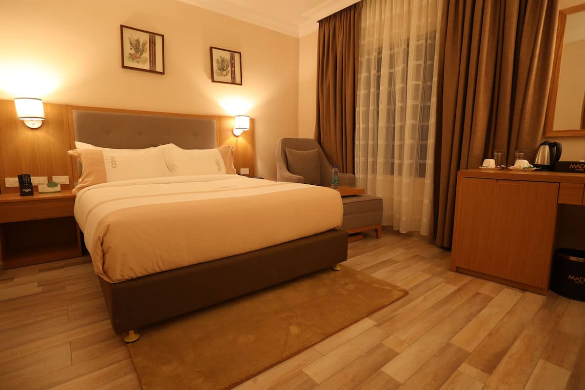 A hotel room with a large bed, bedside tables, a desk, a chair, and a wardrobe.