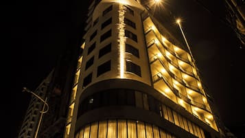 A modern hotel with a curved facade, illuminated signage, and a prominent entrance.