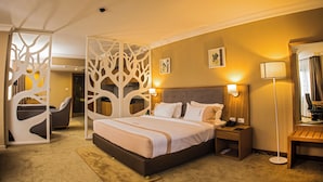 Una habitación de hotel con una cama grande, mesitas de noche, una silla, un escritorio y un separador decorativo.