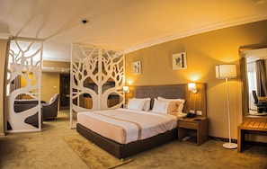 A hotel room with a large bed, bedside tables, a chair, a desk, and a decorative partition. - Mado Hotel (Addis Ababa)