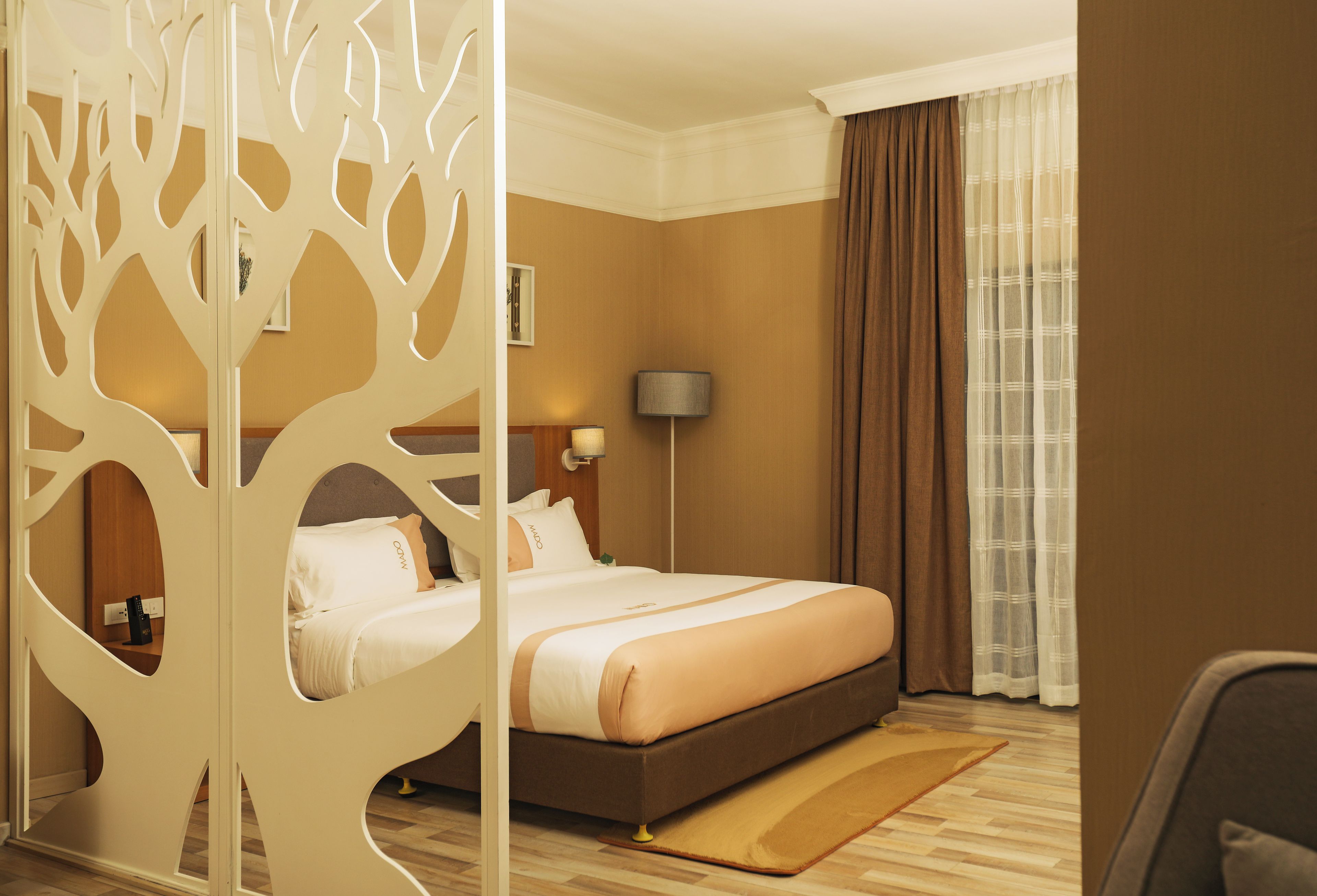 A hotel room with a bed, a nightstand, a lamp, and a window with curtains.