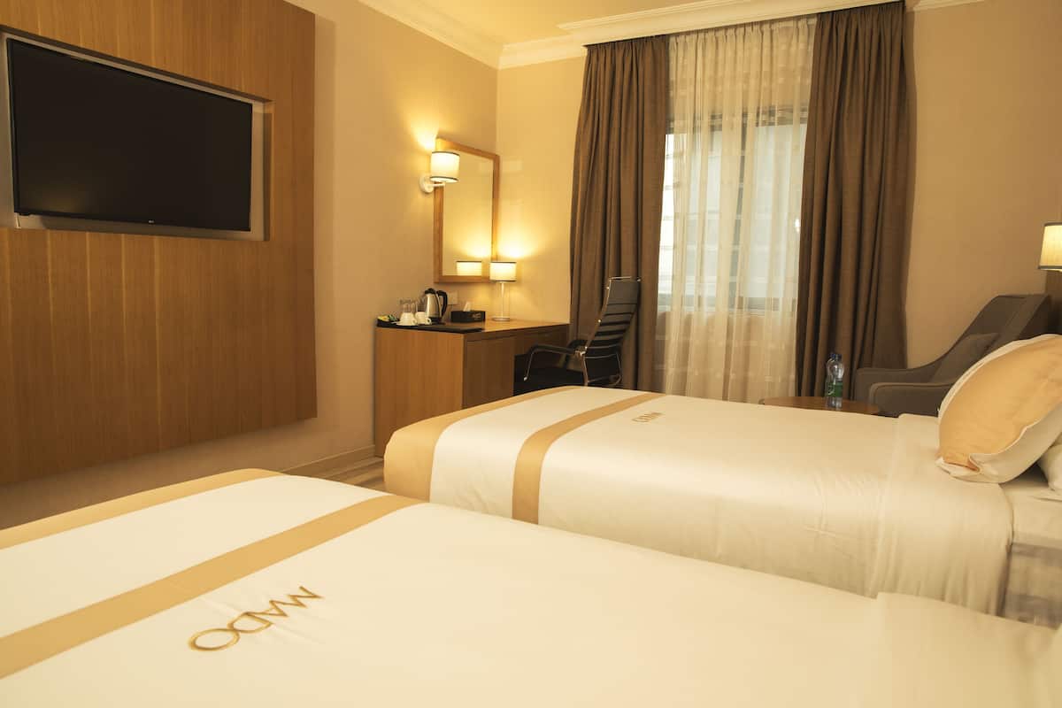 A hotel room with two beds, a TV, a desk with a chair, a mirror, and a window with curtains.