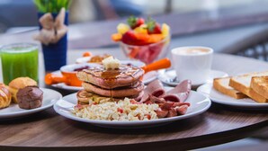 Una mesa de desayuno con tortitas, huevos revueltos, salchichas, tostadas y un bol de fruta.