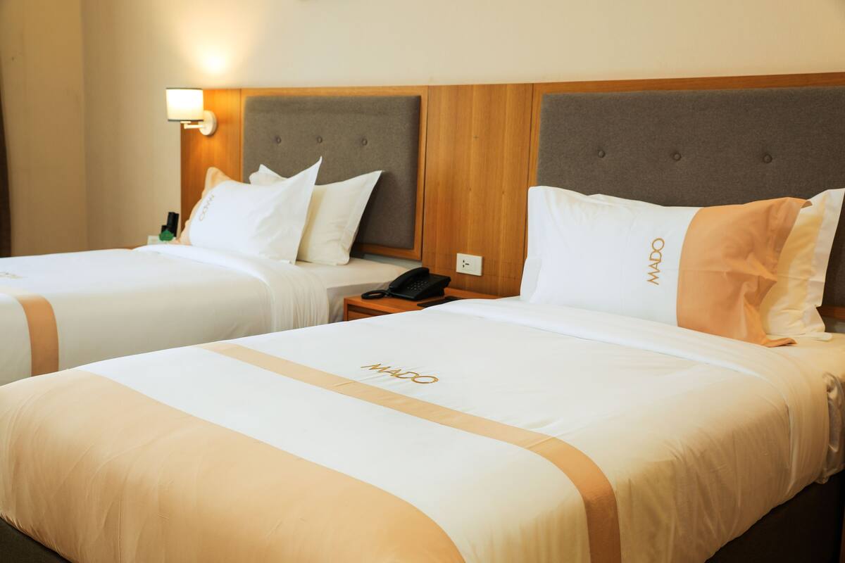 Two hotel beds with headboards, a bedside table with a phone, and a wall-mounted light.