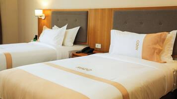 Twee hotelbedden met hoofdeinden, een nachtkastje met telefoon en een wandlamp.