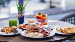 A breakfast spread on a table with croissants, scrambled eggs, sausages, toast, and a fruit bowl. - Mado Hotel (Addis Ababa)
