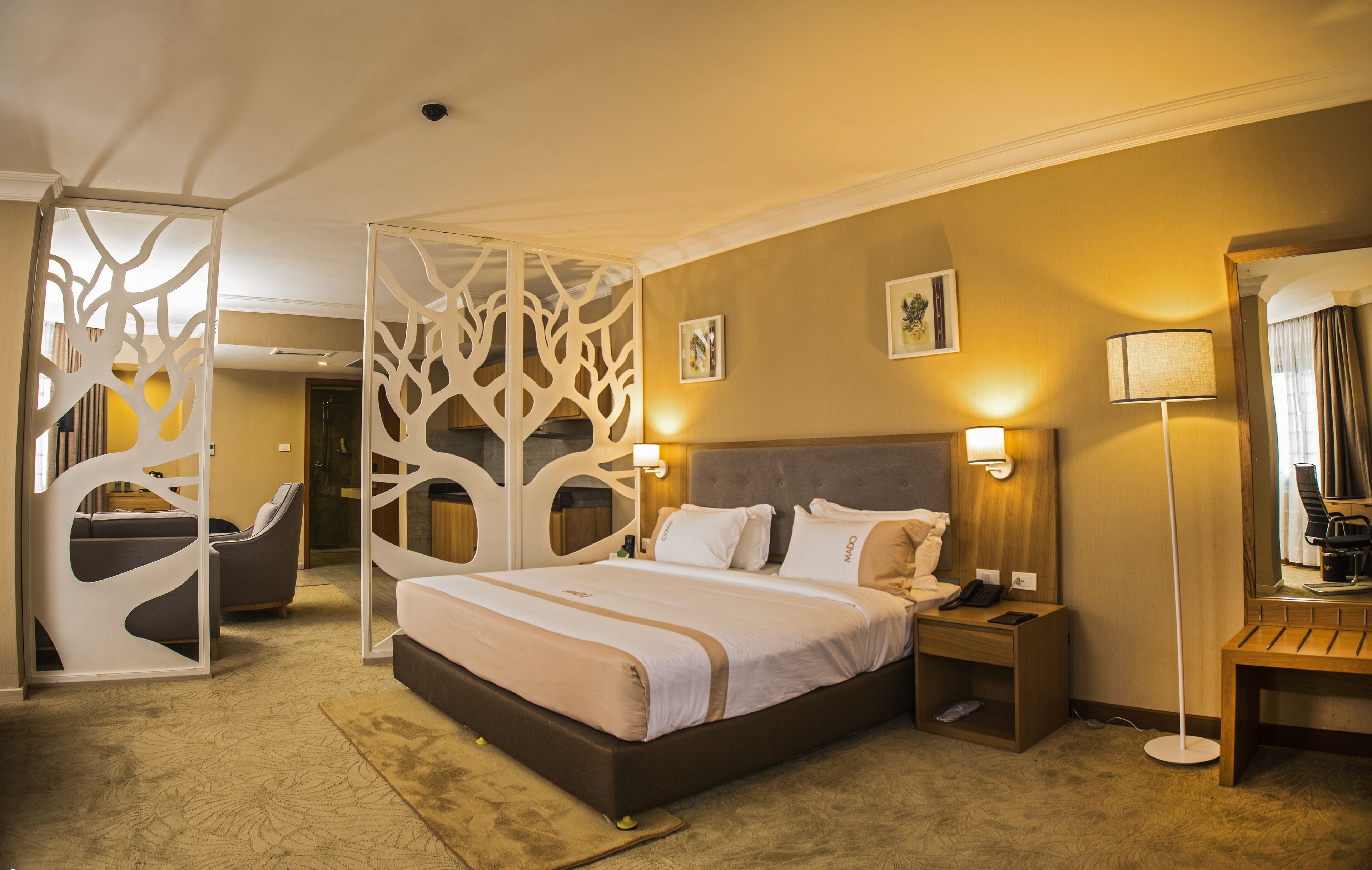 A hotel room with a bed, bedside table, lamp, and a decorative partition.