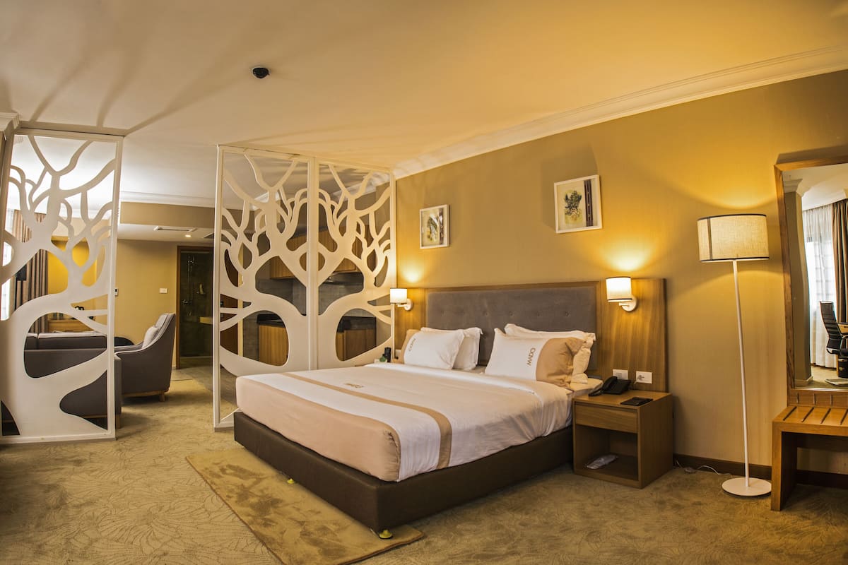 A hotel room with a bed, bedside table, lamp, and a decorative partition.