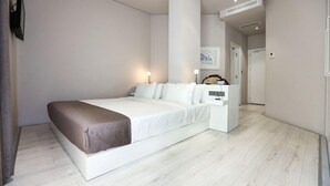 A modern hotel room with a large bed, a bedside table, and a wall-mounted lamp.