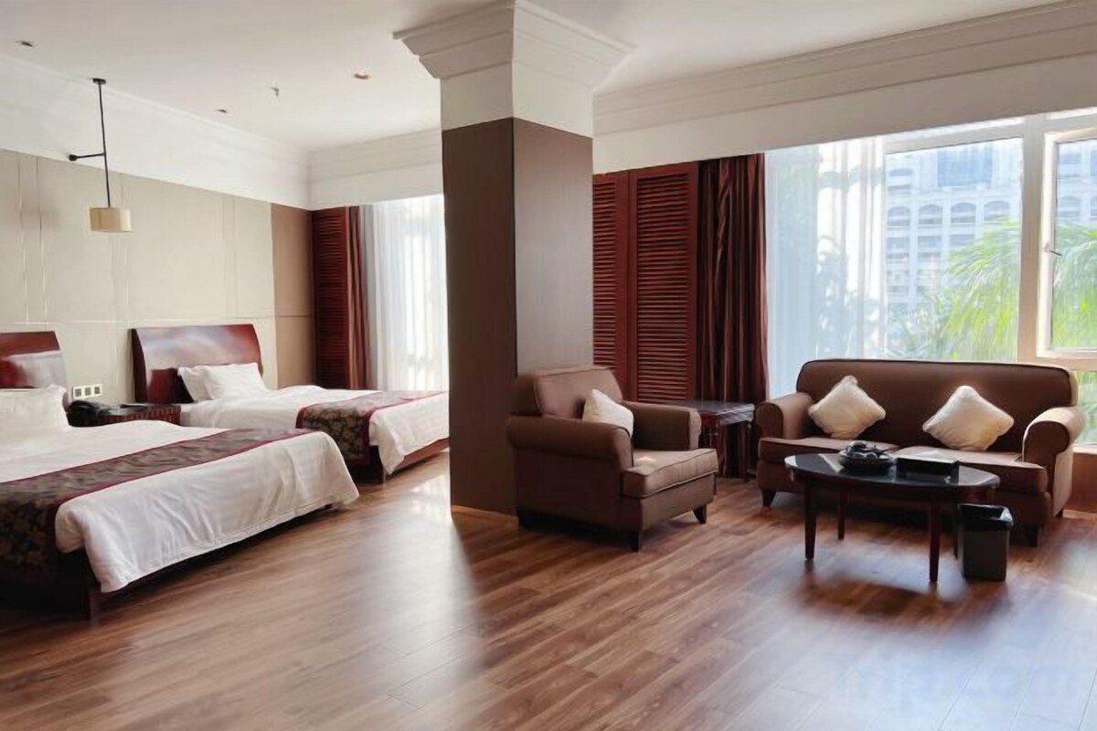 A hotel room with two beds, a sofa, a coffee table, and large windows.