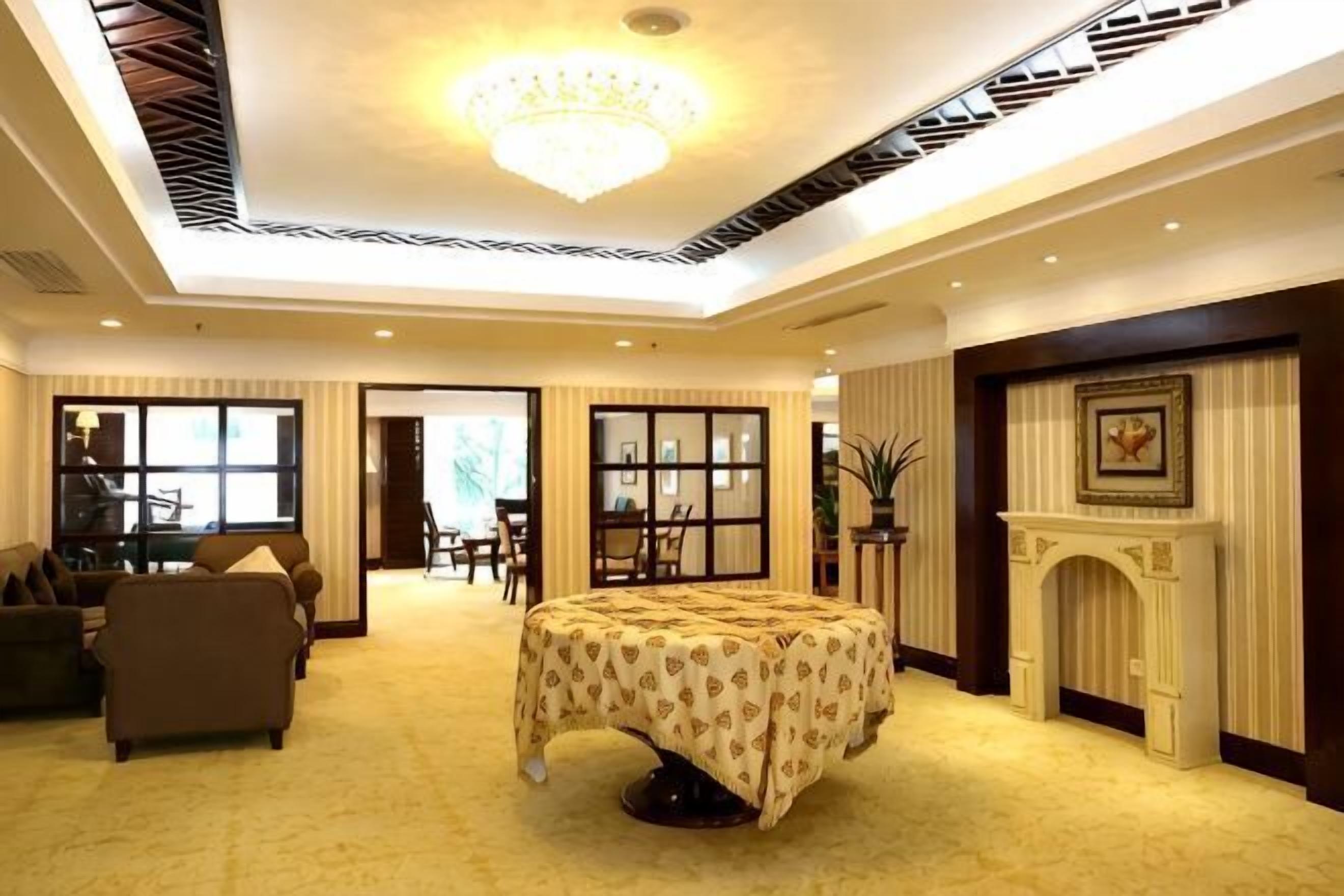 A hotel room with a bed, a fireplace, a dining area, and a view through a large window.