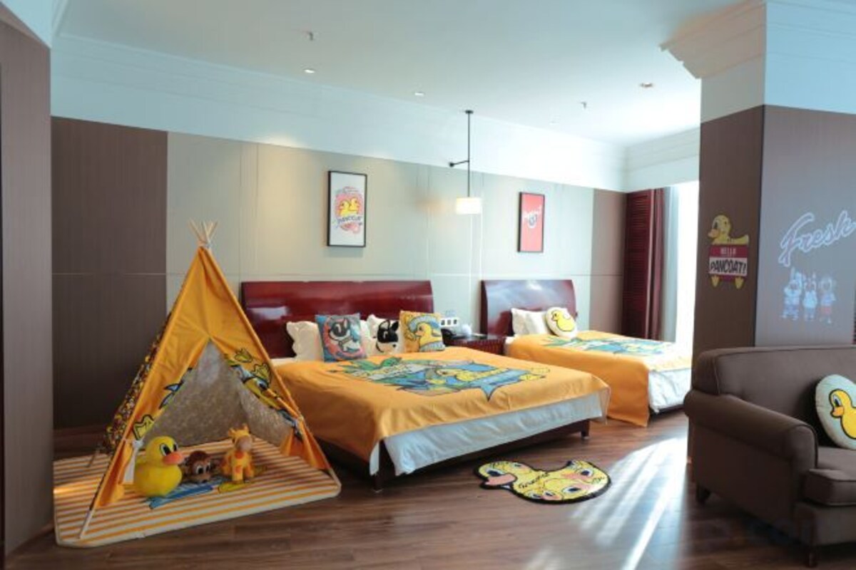 A hotel room with two beds, a sofa, a tent-like play area, and a projector screen.
