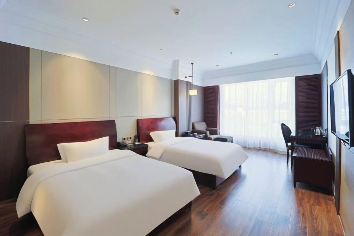 A hotel room with two beds, a desk, and a TV.
