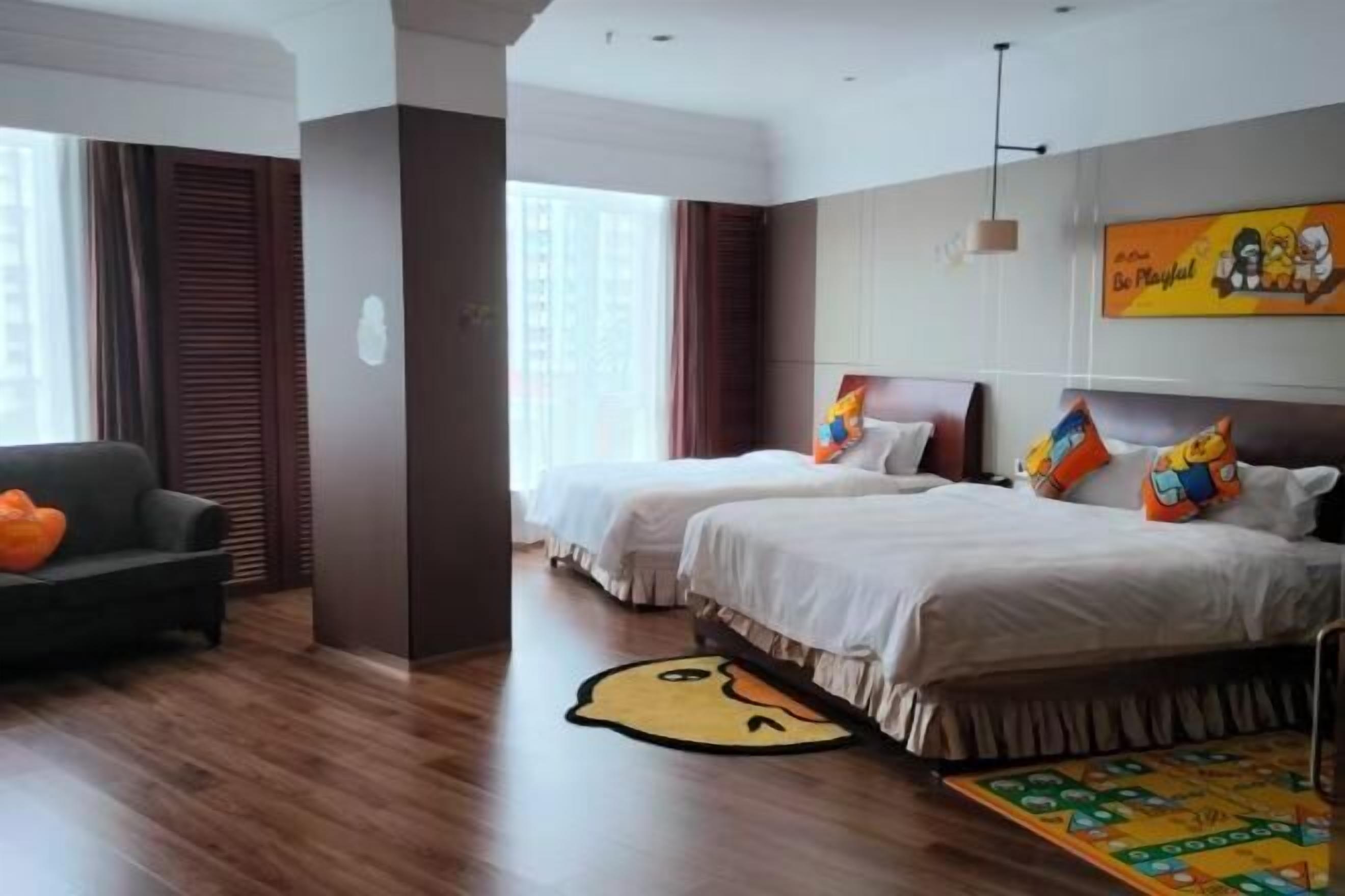 A hotel room with two beds, a sofa, a large window, and a colorful rug.
