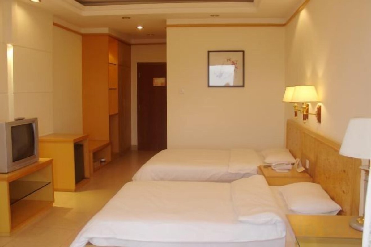 A hotel room with two beds, a television, a desk, and a lamp.