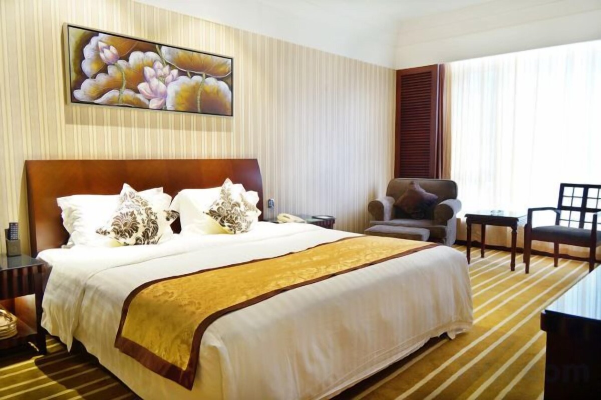A hotel room with a large bed, a chair, a desk, and a window with curtains.