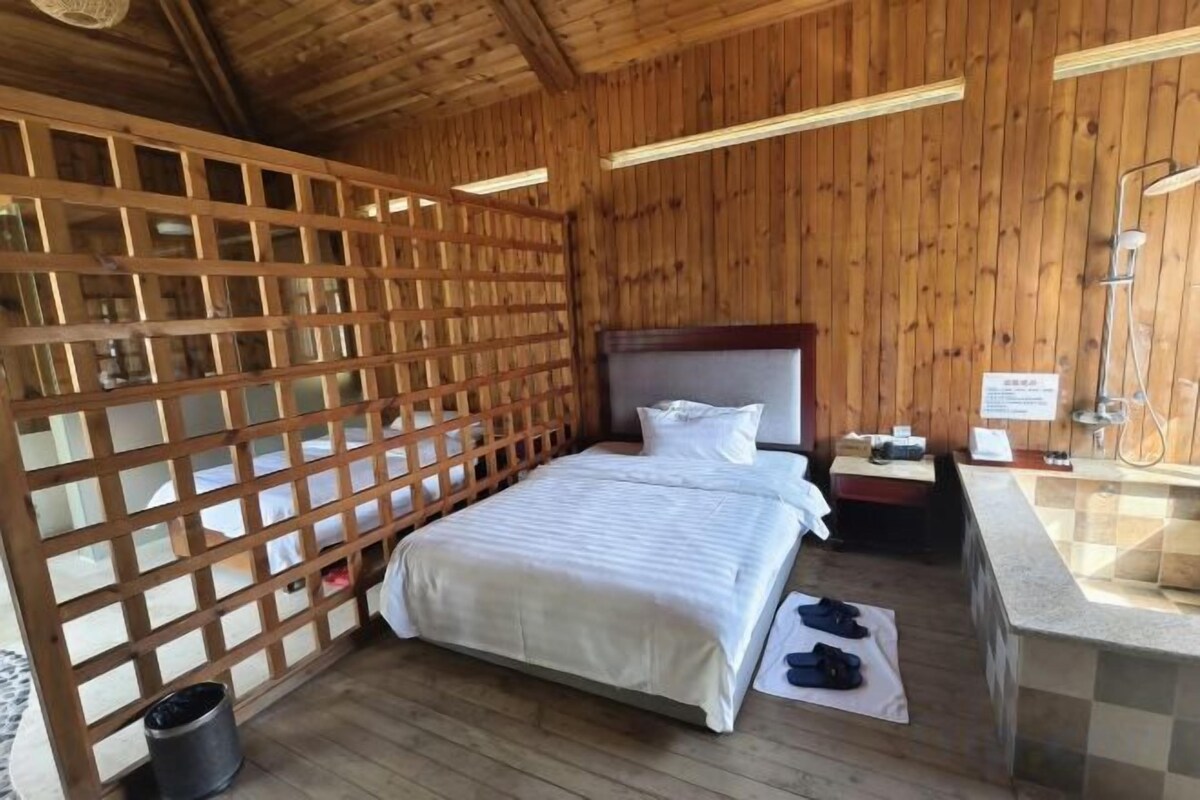 A wooden-paneled room with a bed, a nightstand, a sink, and a shower area.