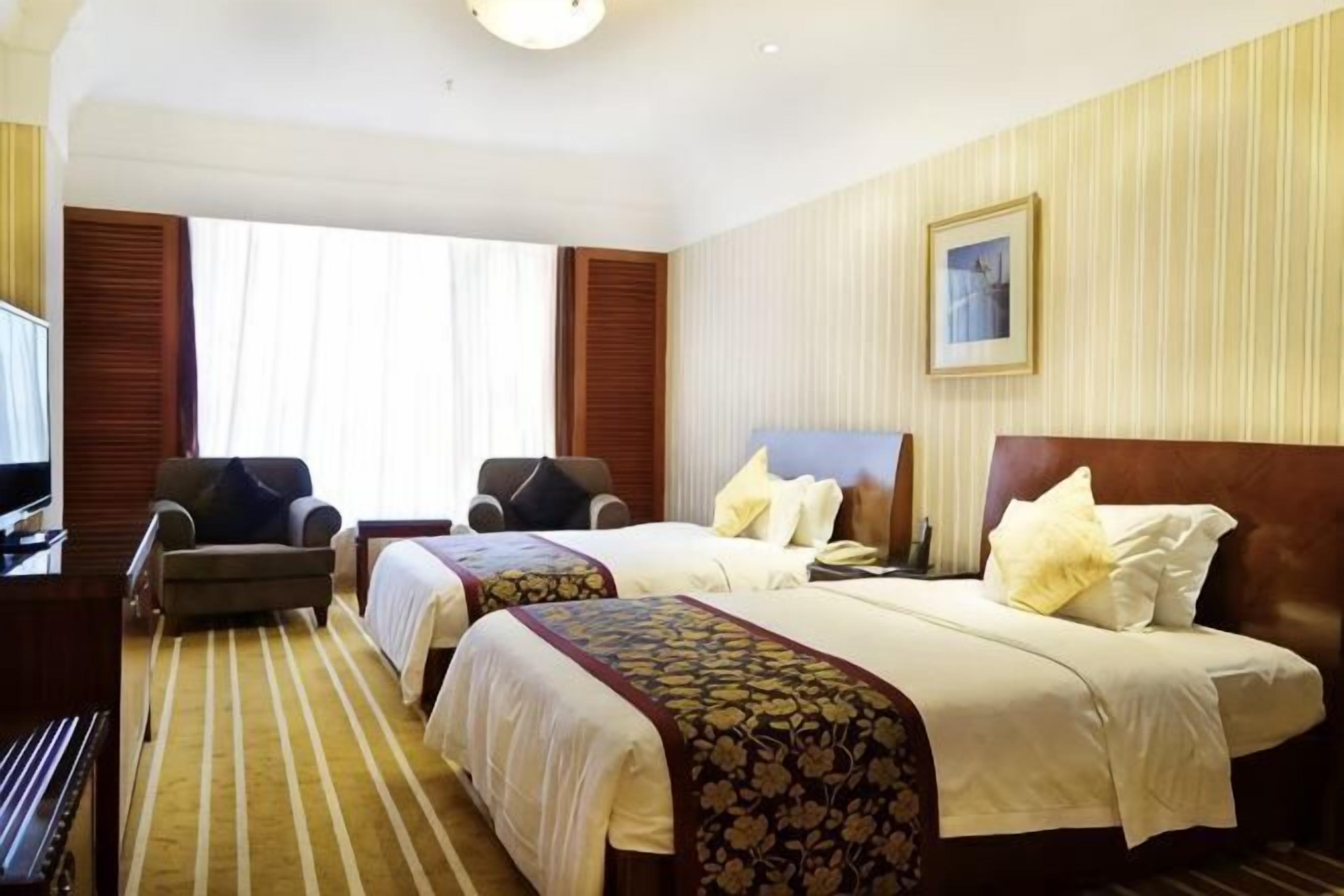 A hotel room with two beds, a desk, a chair, and a television.