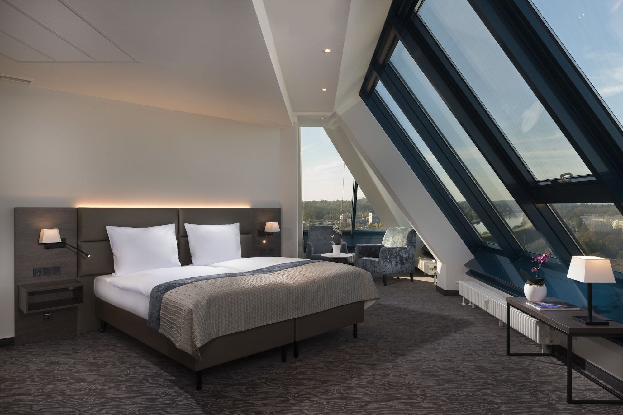 A modern hotel room with a large bed, a seating area with a view, and a skylight.