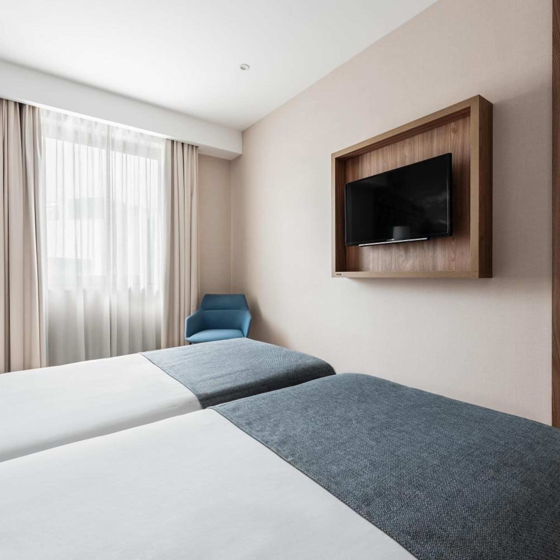 Una habitación de hotel con dos camas, un televisor montado en la pared y una silla.