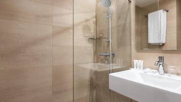 A modern bathroom with a glass-enclosed shower, a white sink, and a mirror above it.