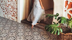Une femme vêtue d’une robe à rayures traverse un portail orné, qui donne sur un sol à motifs et un mur décoratif.