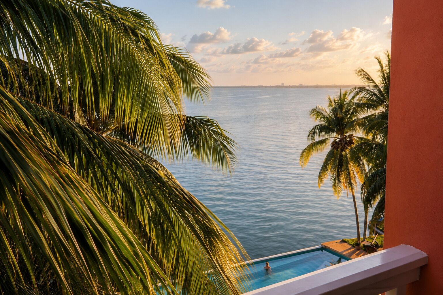 A poolside view with a clear view of the ocean and palm trees.
