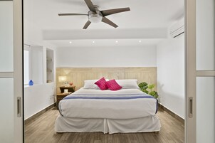 A modern hotel room with a large bed, a ceiling fan, a bedside table, and a nightstand.