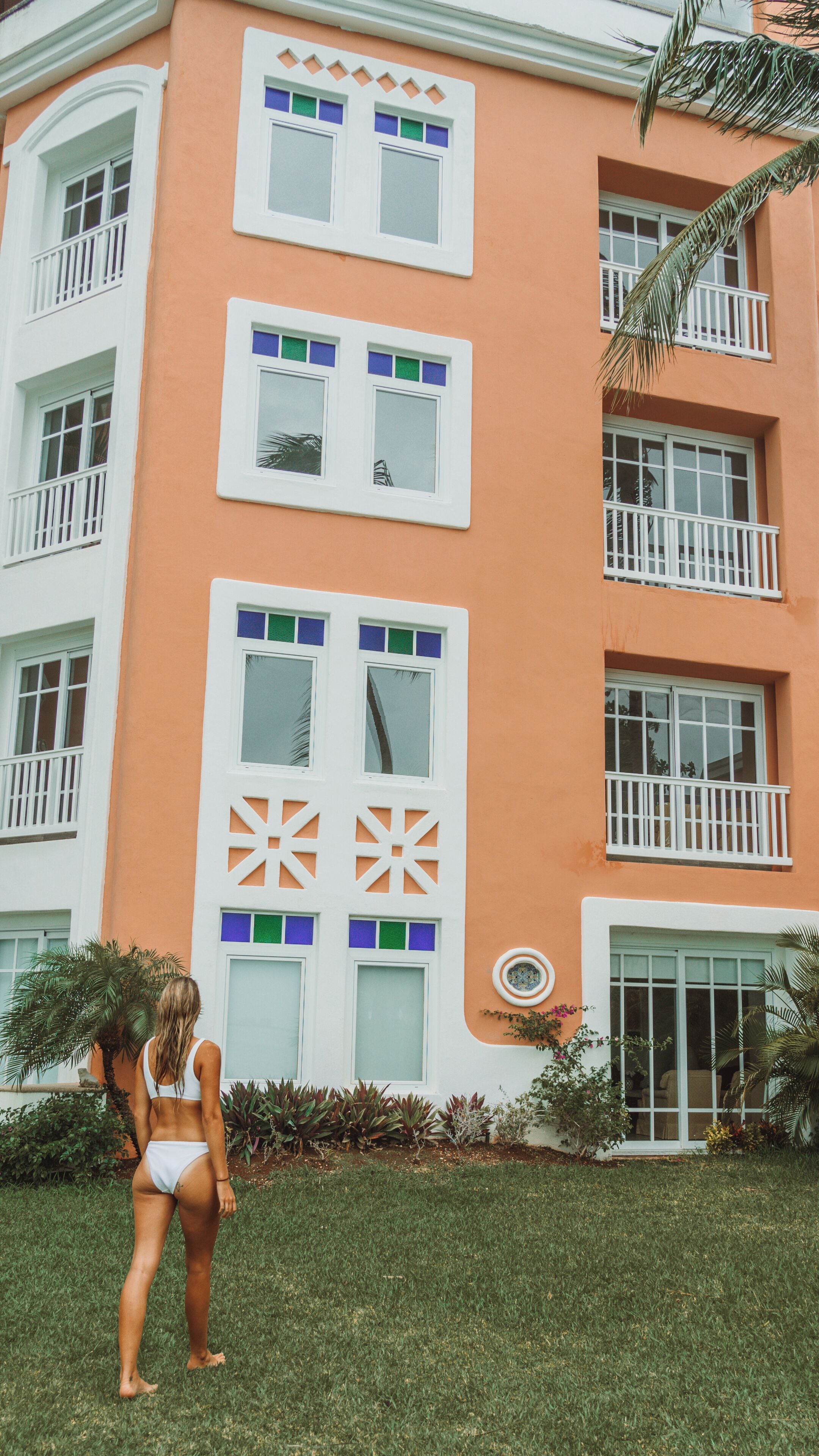 Un edificio de varios pisos con balcones, un amplio acceso por puerta de vidrio y un césped cuidado.