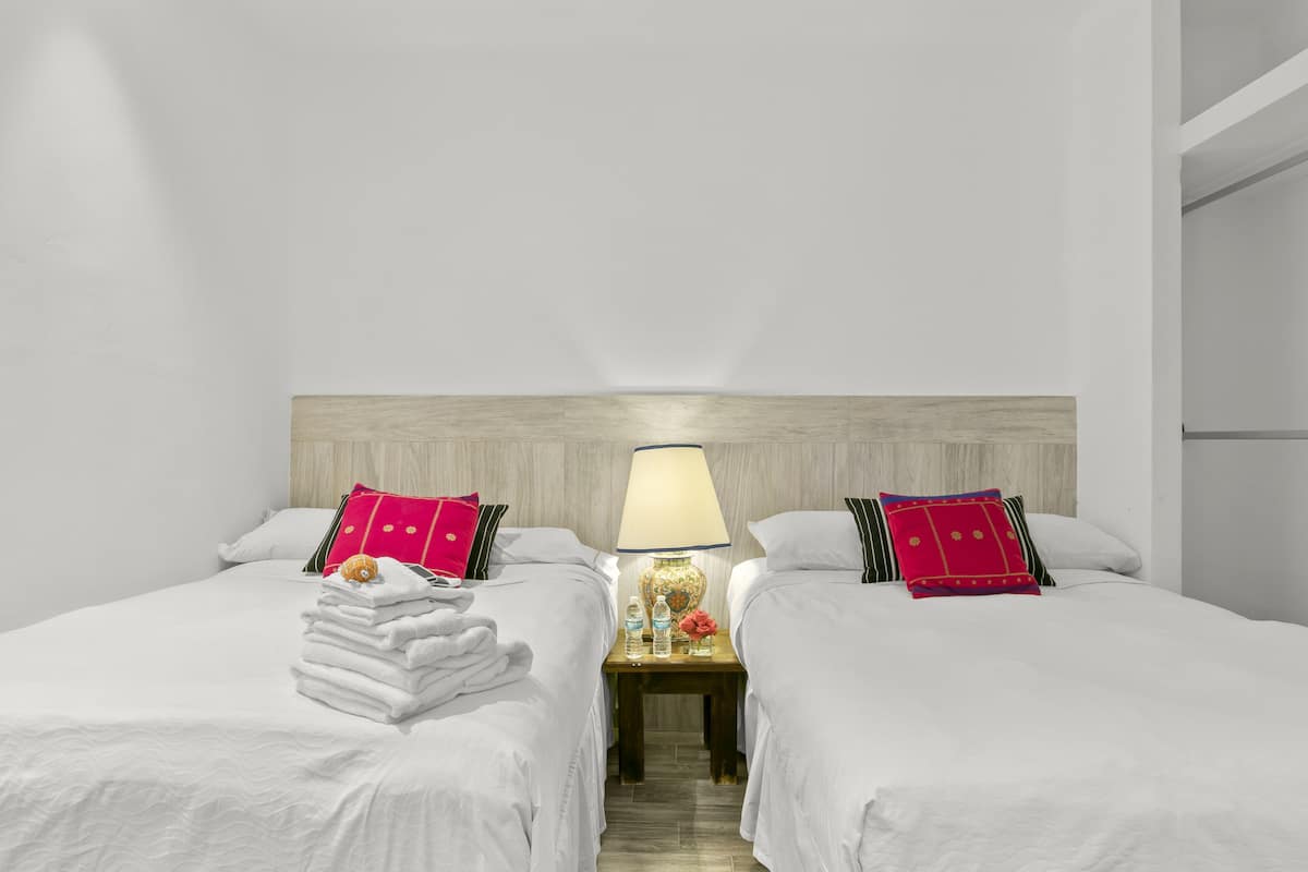 Una habitación de hotel con dos camas, una mesita de noche con lámpara y un cabecero de madera.