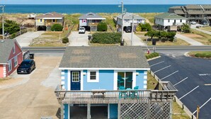 A coastal building with a small deck, a garage, and a parking lot. - Gypsea Wind: Oceanside, Short Walk to Beach, Short Stays Anytime! (Kill Devil Hills)