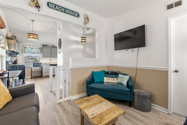A living room with a teal sofa, a wooden coffee table, and a television mounted on the wall.