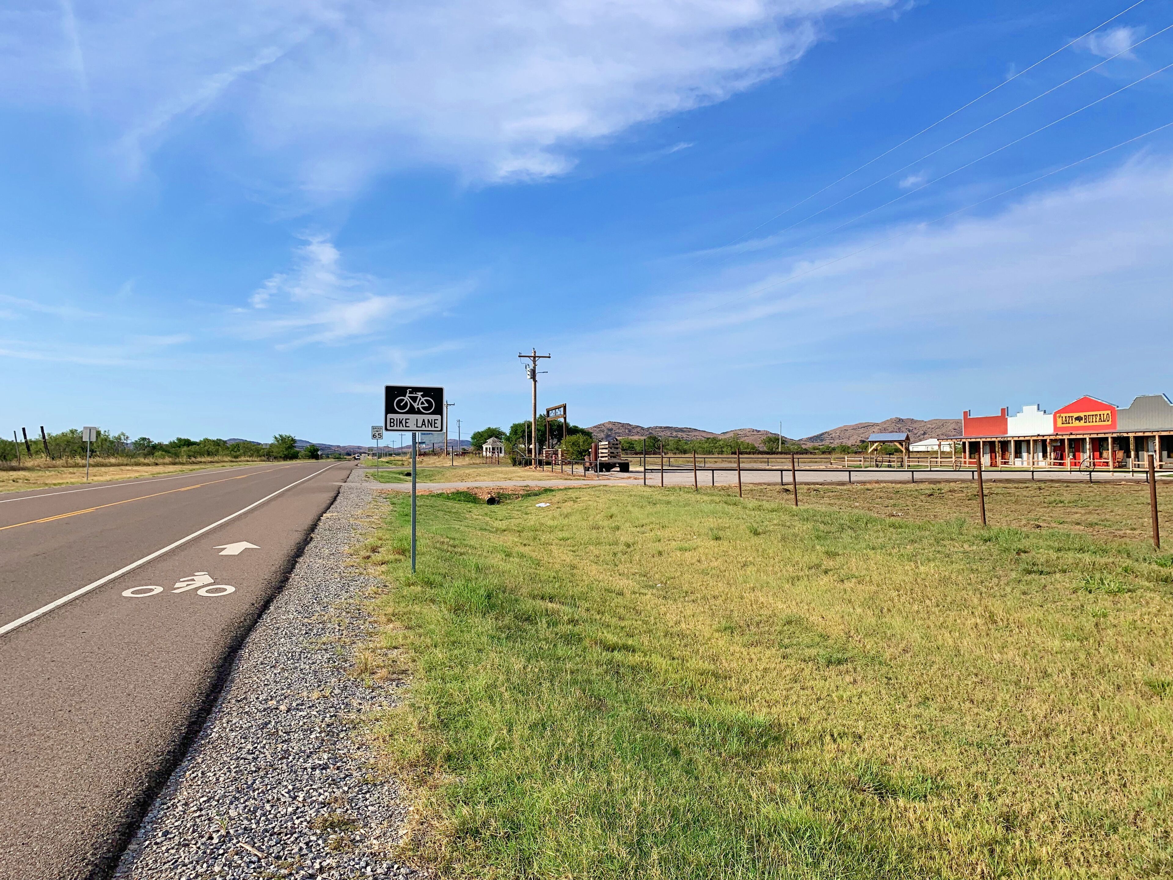 A rural road with a bike lane sign, a gravel shoulder, and a building with a red and white facade.