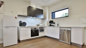 A modern kitchen with white cabinetry, a built-in oven, microwave, and dishwasher. - Quality Apartments Dandenong (Dandenong)