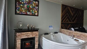 A bathroom with a stone fireplace, a large bathtub, and a colorful abstract painting on the wall. - Yellow Tree Suites (La Fortuna)