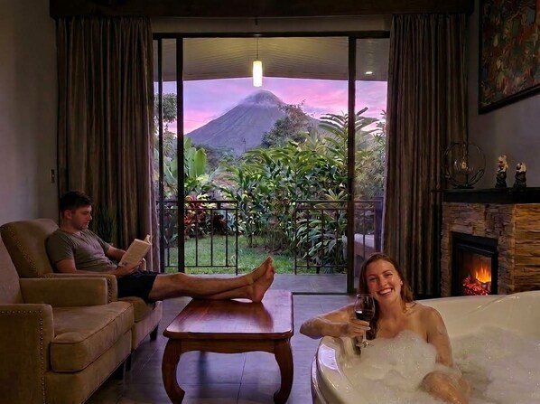 A room with a glass door leading to a balcony, a fireplace, and a bathtub with bubbles. - Yellow Tree Suites (La Fortuna)