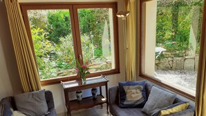 Una stanza accogliente con un divano grigio, un tavolino in legno con un vaso di fiori e vista su un giardino attraverso un'ampia finestra.