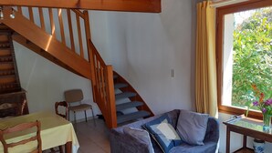 Un soggiorno accogliente con una scala in legno, un'area pranzo con tavolo e sedie, e una finestra vista sul verde.