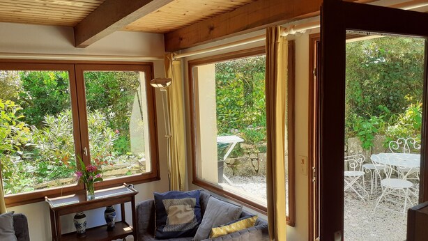 Una camera accogliente con una panca imbottita, un tavolino con un vaso e vista su un giardino esterno attraverso ampie finestre.