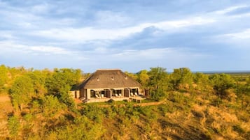 A single-story building with a thatched roof, surrounded by dense vegetation, and a clear sky above.